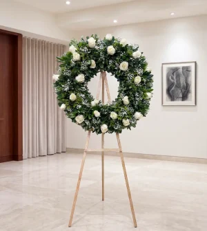 Elige coronas de flores para muertos con 24 rosas blancas y flores nubecitas, ideales para expresar un pésame lleno de paz y respeto.